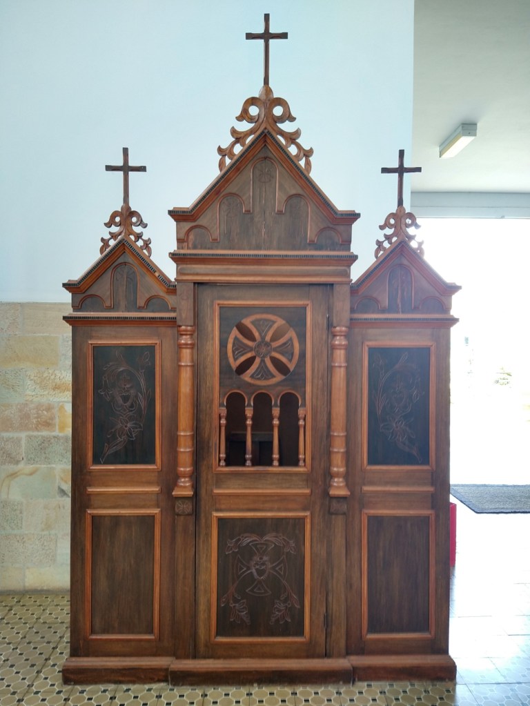 confessionário feito de madeira, local destinado às confissões. Seu desenho visa garantir a privacidade e a confidencialidade do ato sacramental, diminuindo a intimidade física. Uma tela separa o padre e o penitente, garantindo o anonimato.